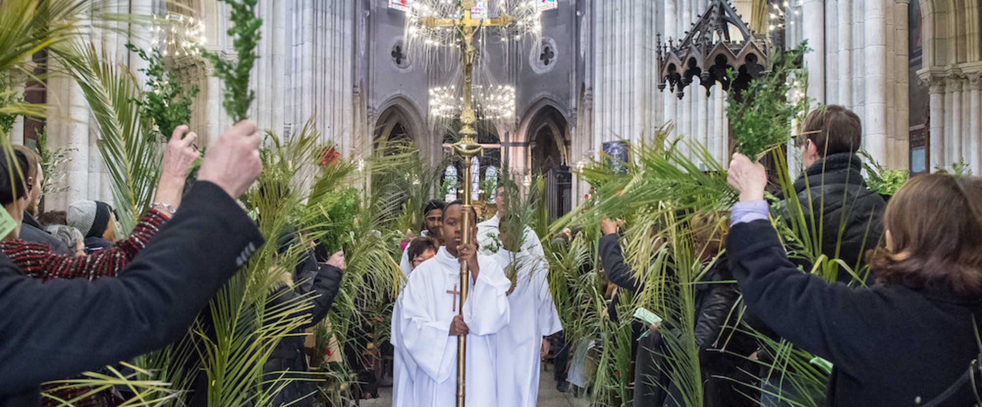 Messdiener laufen durch den mit Palmblättern geschmückten Mittelgang der Kirche Saint-Jean-Baptiste de Belleville in Paris nach dem Palmsonntagsgottesdienst am 25. März 2018. Menschen halten Palmzweige in die Höhe, ein Ministrant trägt ein goldenes K